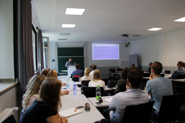 Mehrere Personen in einem Seminarraum gucken zu einer Leinwand